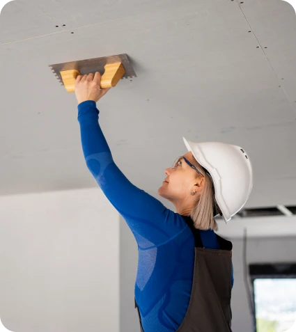 Reparacion de Goteras 3 Mujer trabajadora con casco aplicando yeso en el techo durante una renovación, utilizando una llana en un entorno de construcción
