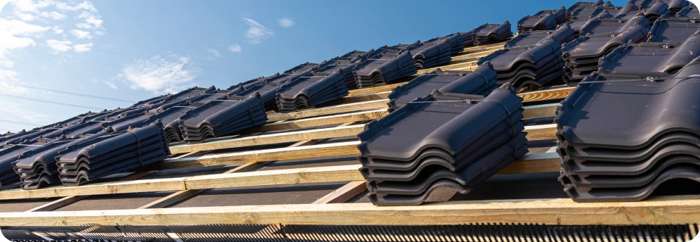 Construcción de Tejados 5 Tejas negras apiladas sobre una estructura de madera durante la construcción de un tejado bajo un cielo despejado