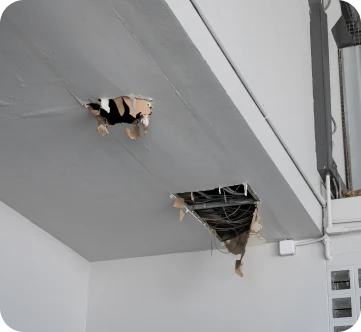 Construcción de Tejados 2 Techo interior con daños visibles, mostrando agujeros grandes y cables expuestos en una construcción en proceso de reparación