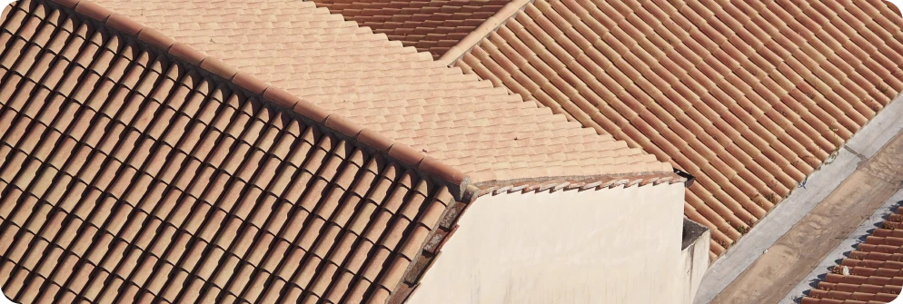 Reformas Integrales 1 Tejados inclinados de tejas de barro rojo, mostrando múltiples niveles de techos tradicionales en un edificio bajo un cielo despejado
