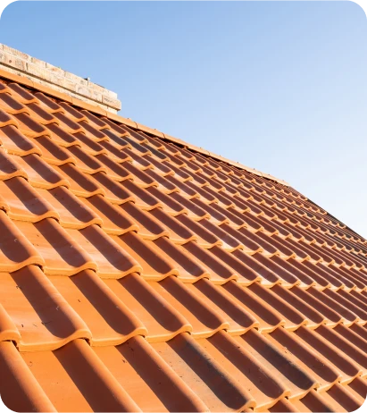 Construcción de Tejados 7 Tejado inclinado de tejas de arcilla roja recién colocadas bajo un cielo azul despejado, mostrando un patrón simétrico y pulido