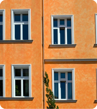 Reformas Integrales 7 Fachada de edificio con paredes naranjas y ventanas blancas de estilo moderno, iluminada por la luz del sol en un día despejado