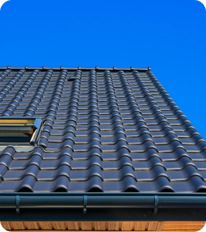 Construcción de Tejados 9 Tejado inclinado de tejas negras brillantes con una ventana instalada bajo un cielo azul claro, mostrando un diseño moderno y limpio