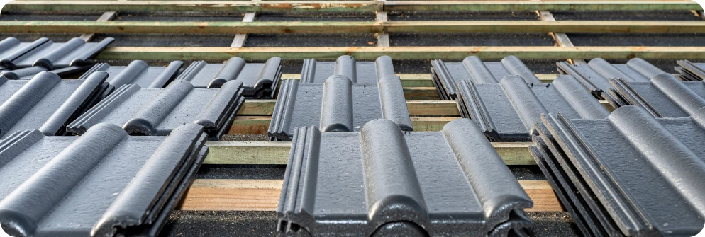 Reparacion de Goteras 1 Tejas nuevas de color gris oscuro listas para ser instaladas en un tejado durante un proceso de construcción o reparación de techos