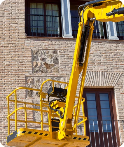 Reformas Integrales 3 Plataforma elevadora amarilla utilizada para trabajos de mantenimiento en la fachada de un edificio de ladrillo bajo un cielo despejado