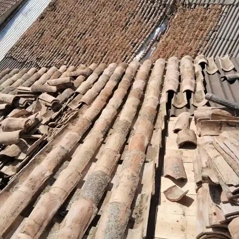 Tejado en reparación con tejas antiguas removidas y tejas nuevas listas para instalar.